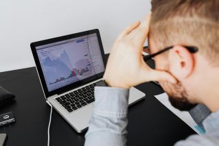 Over the shoulder view of a man analyzing financial data on a laptop screen.