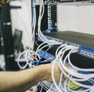 An IT professional configuring network cables in a server rack, focusing on Ethernet connections.